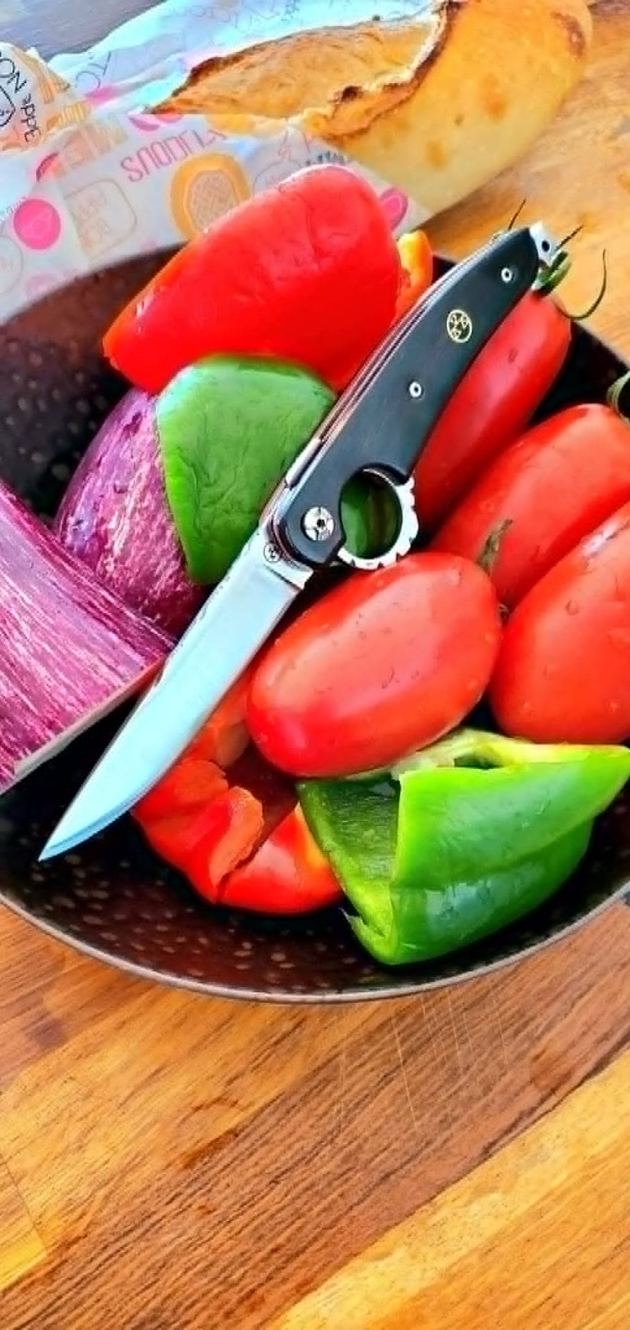 Le Fhiers with a black handle resting on market vegetables, blade open, reverse-opening ring visible.