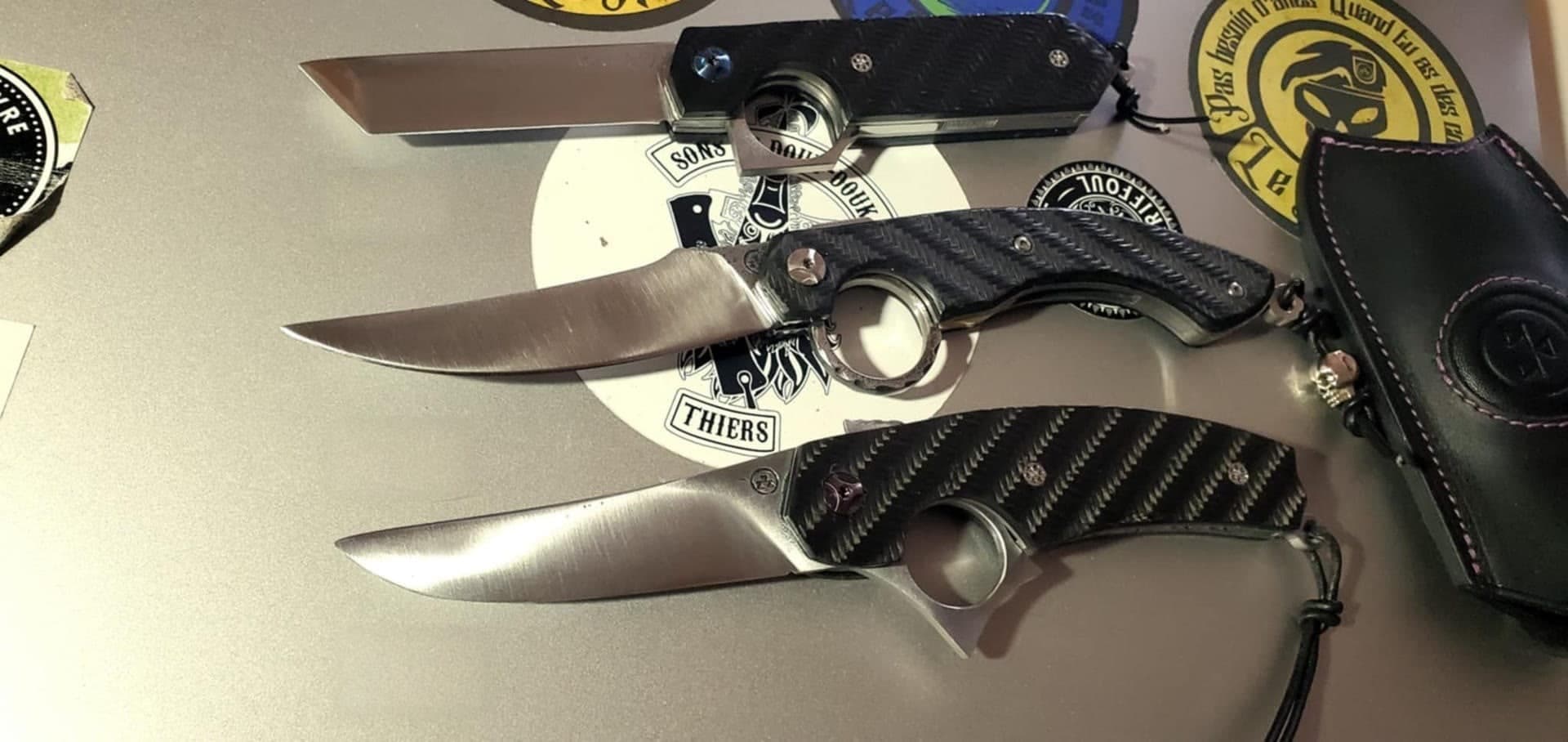 Three Résiliant knives with woven carbon fibre handles, two of them open, laid out on the display at the Thiers workshop.