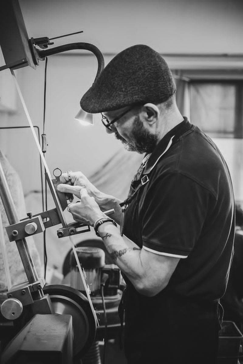 Le coutelier du Résiliant au backstand, concentré sur l'émouture d'une lame dans l'atelier de Thiers, photo en noir et blanc.
