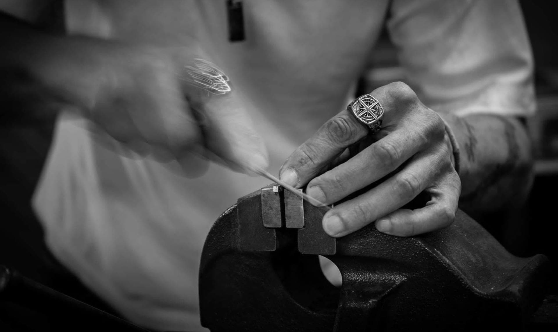 Precision work at the vise in Le Résiliant's workshop: the cutler's hands adjusting a part, black and white photograph.