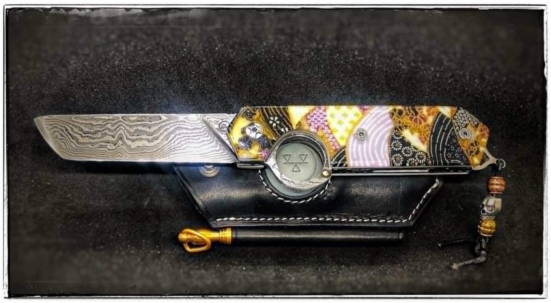 Le Résiliant Tanto open, damascus blade and reverse-opening ring clearly visible, resting on its black leather sheath.