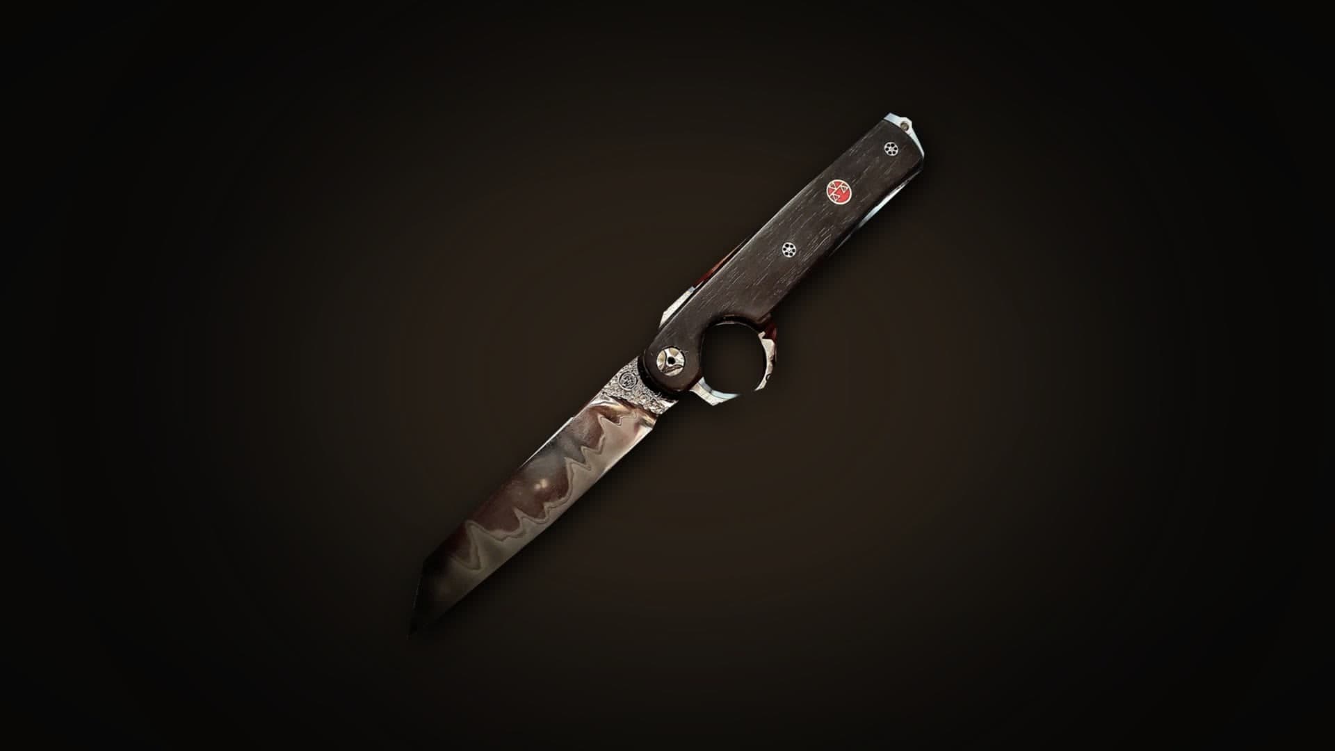 Real photo of the Shotokan, Le Résiliant reverse-opening folding knife: tanto-point blade with its wavy line, dark wood handle with a red inlay, opening ring below the handle, on a dark background.