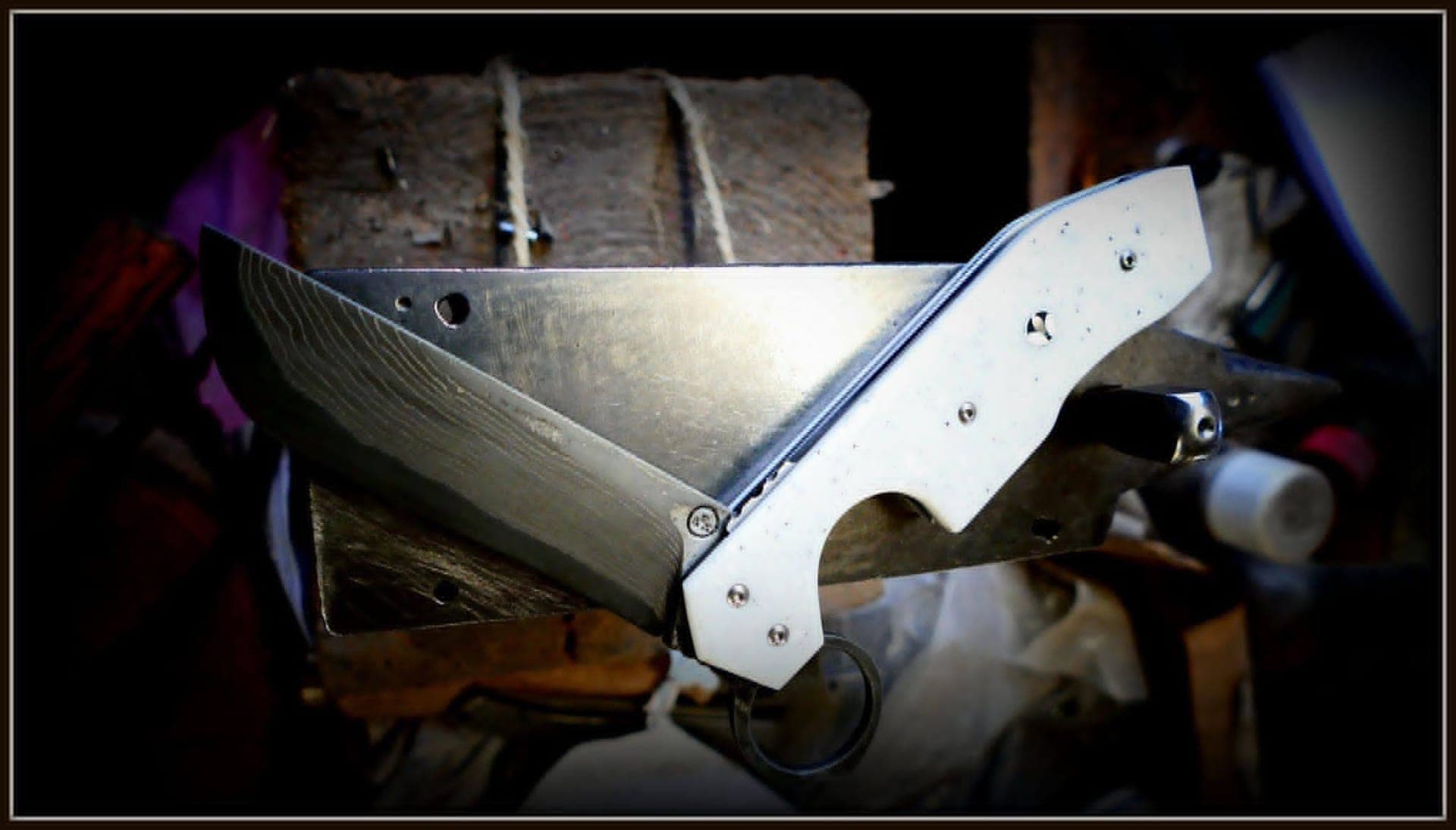Workshop photo: a Résiliant with a damascus blade and a pale handle clamped in the vice, the reverse-opening ring below the handle.